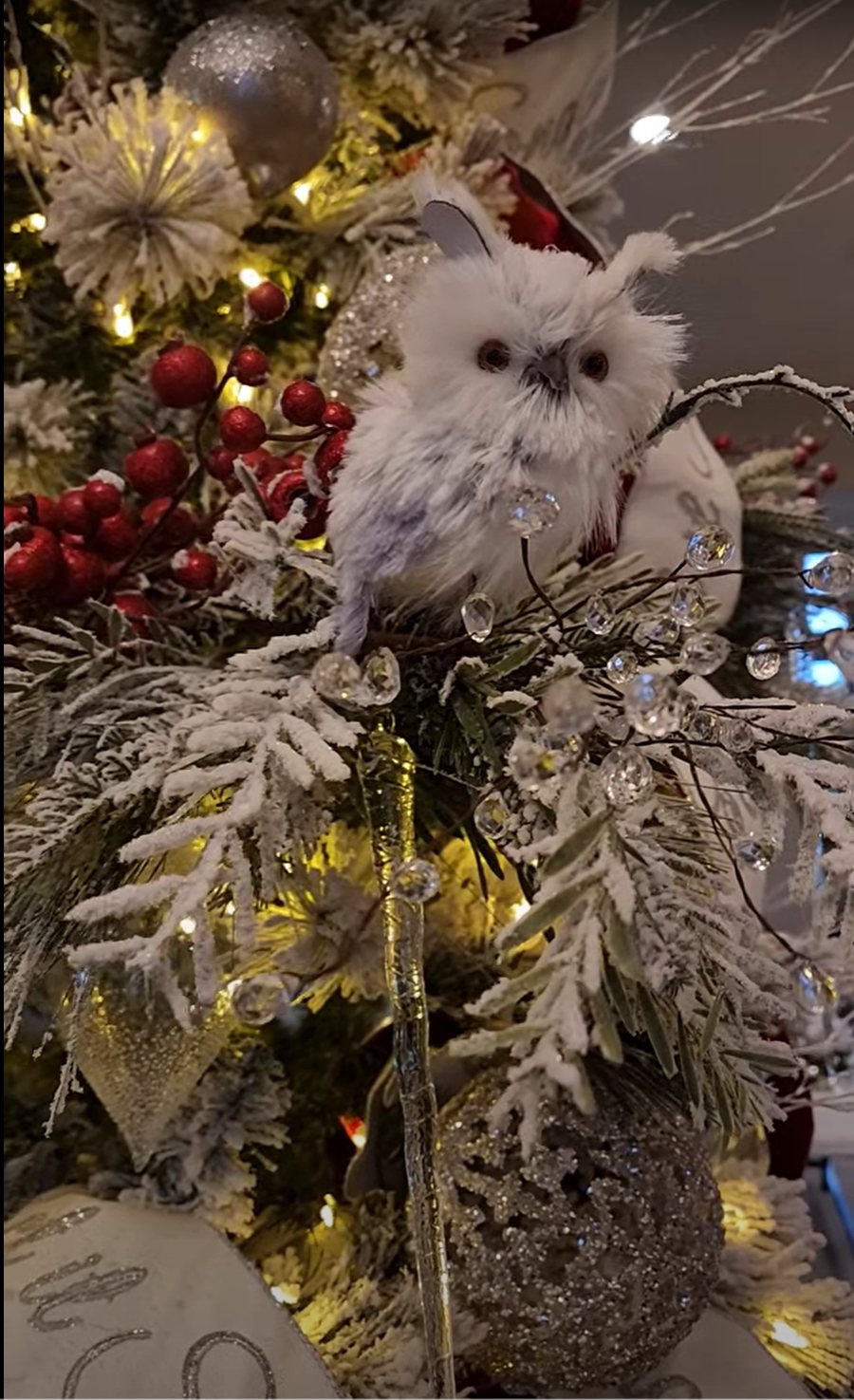 Close-up of a snowy white owl nestled in flocked branches with red berries, crystal sprays and silver ornaments