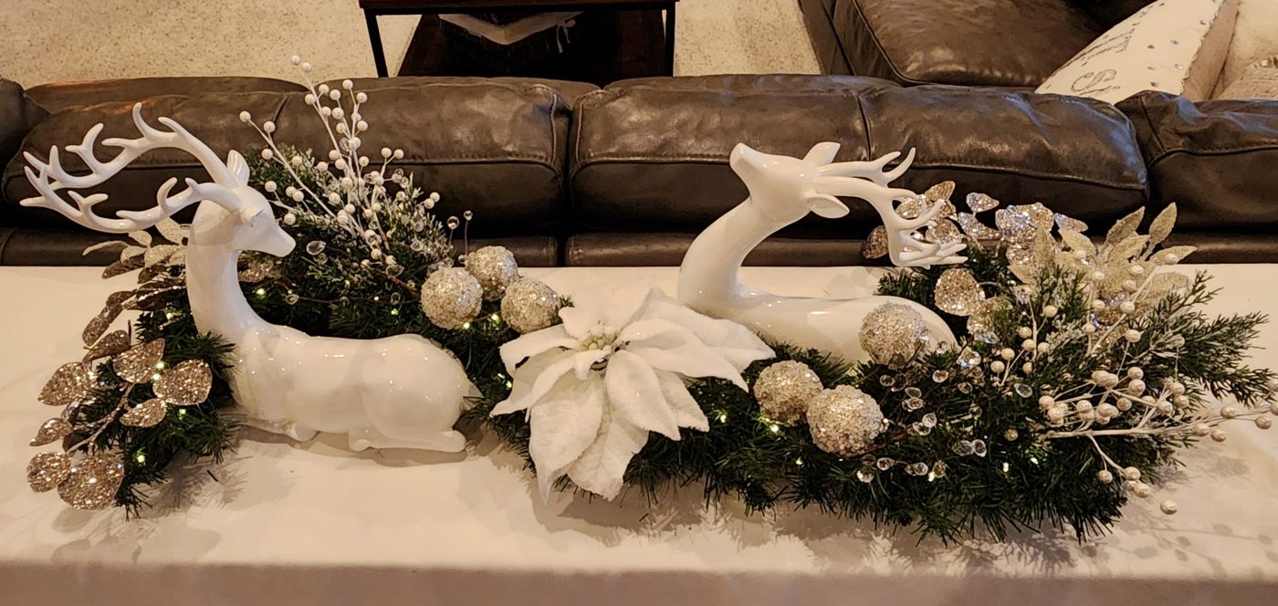 White ceramic reindeer centerpiece with lit greenery, white poinsettia, pearl berries and champagne glitter accents